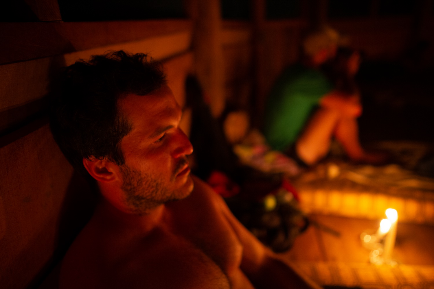 This is a photo of a man, Jesse Gould, in dim candlelight from the side. He is very relaxed, laying down outside, and not wearing a shirt.