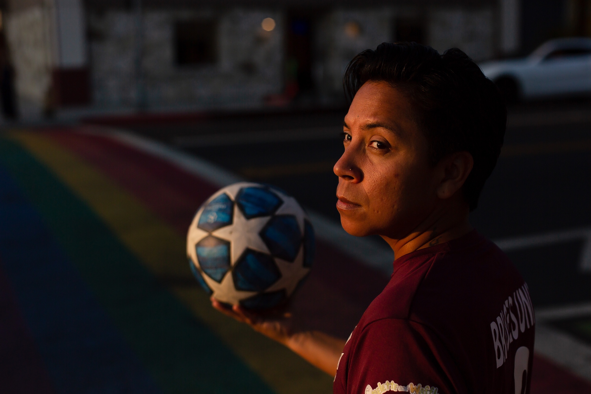 Gael holds a soccer ball in front of a rainbow-painted sidewalk.