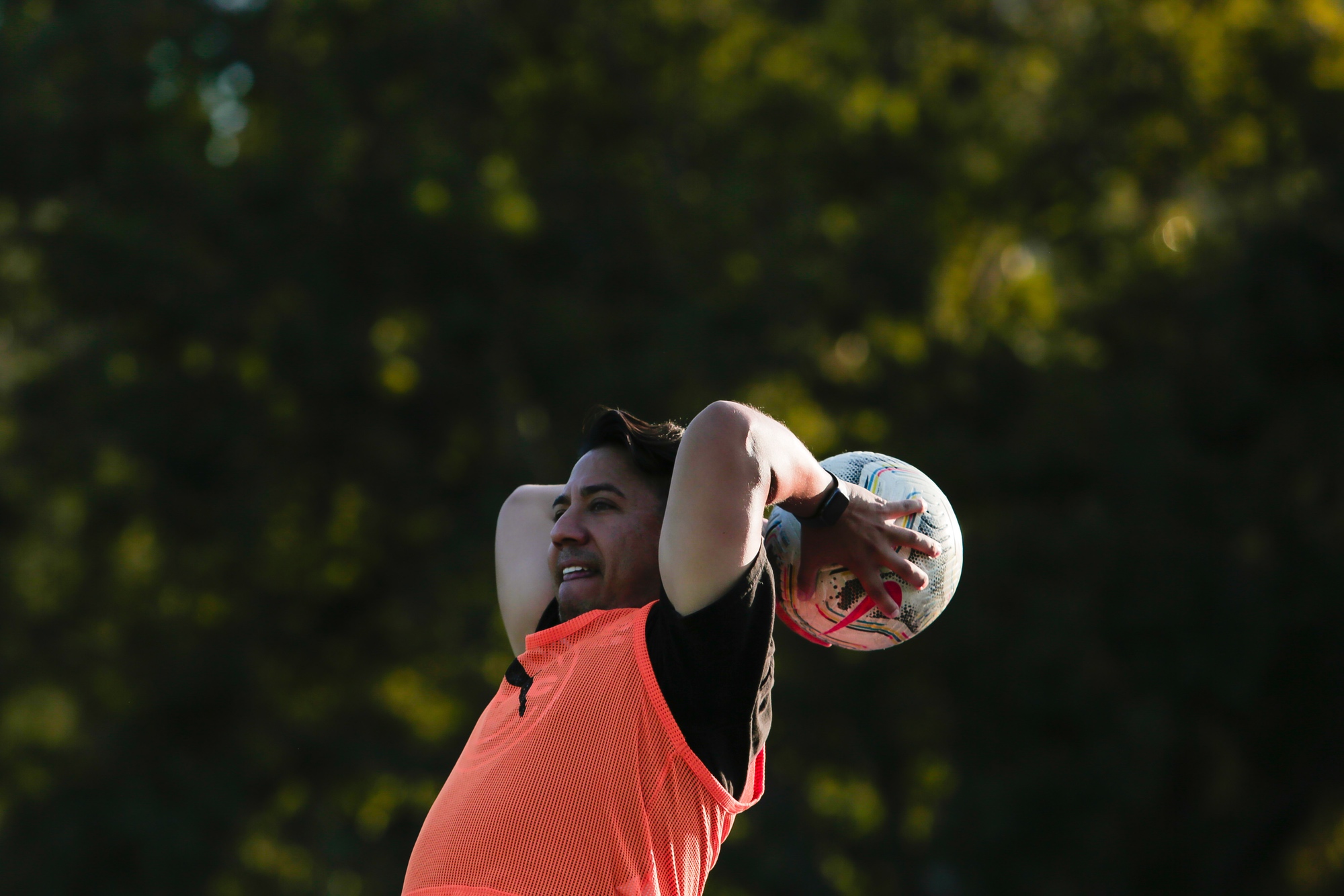 Ken has his hands behind his head, prepared to toss a soccer ball in the park.