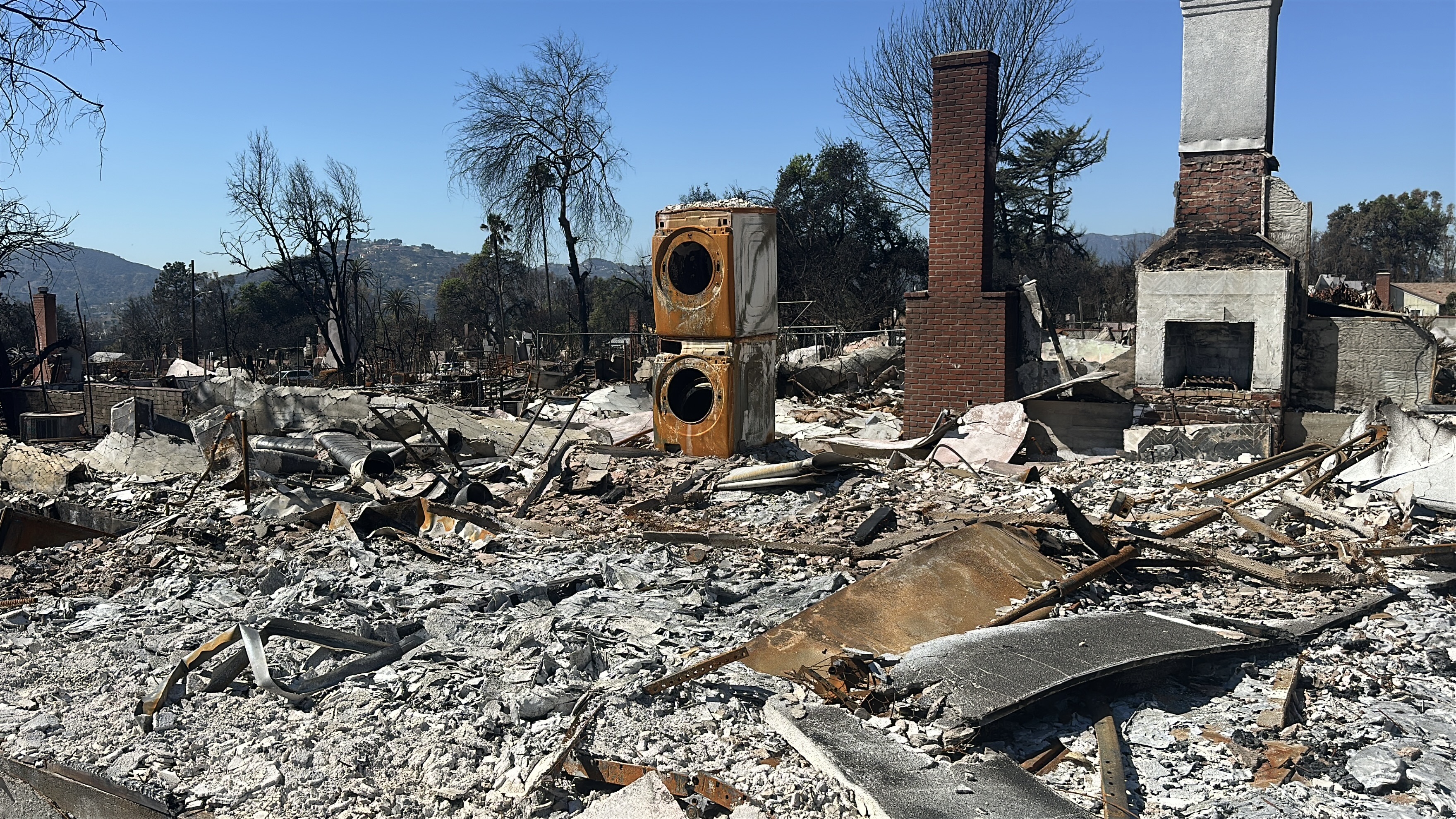 Fire devasation in Altadena. A burned washer and dryer remains standing along with a chimney.