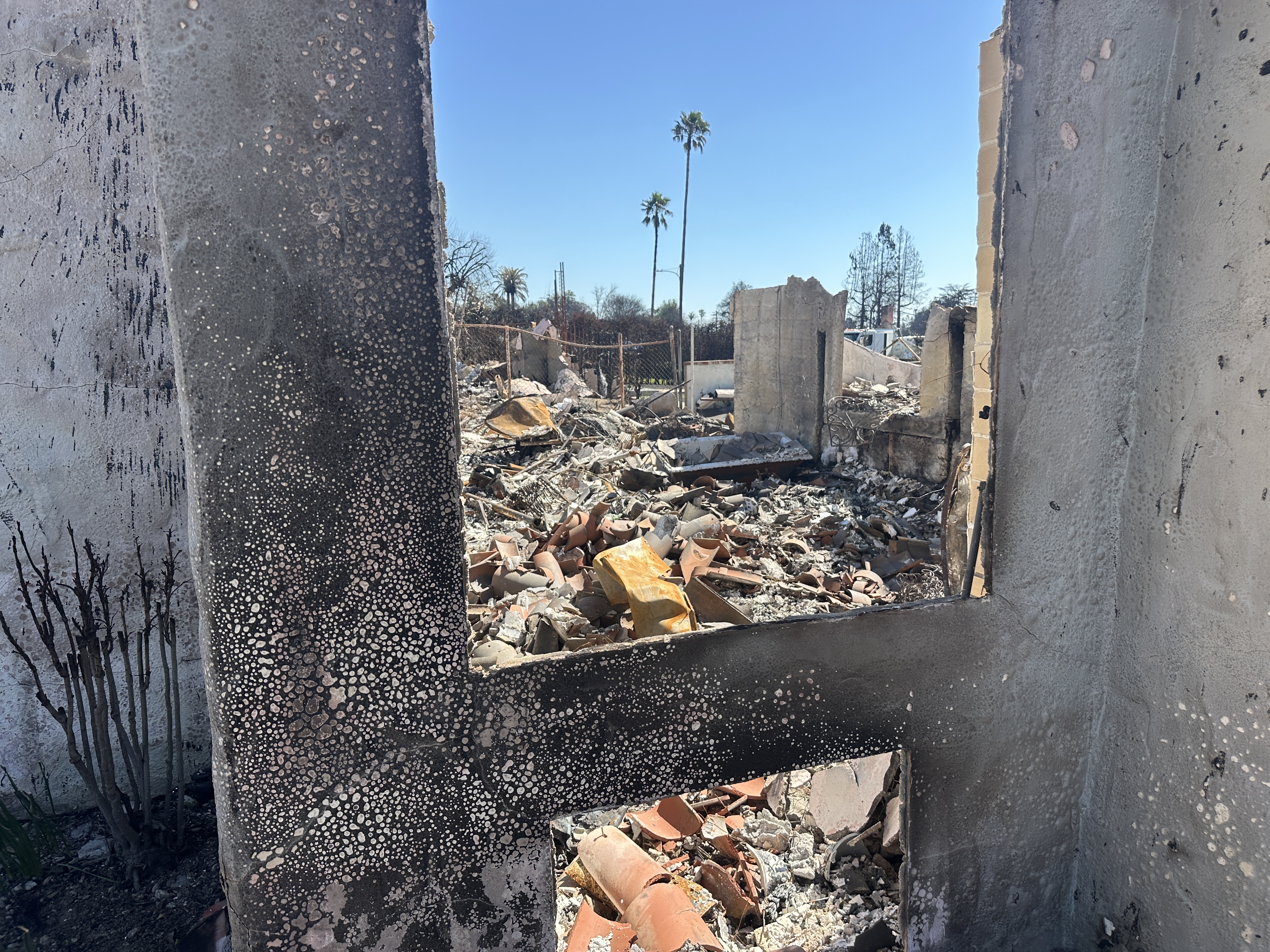 A view of altadena fire devasation through a burned facade of a window